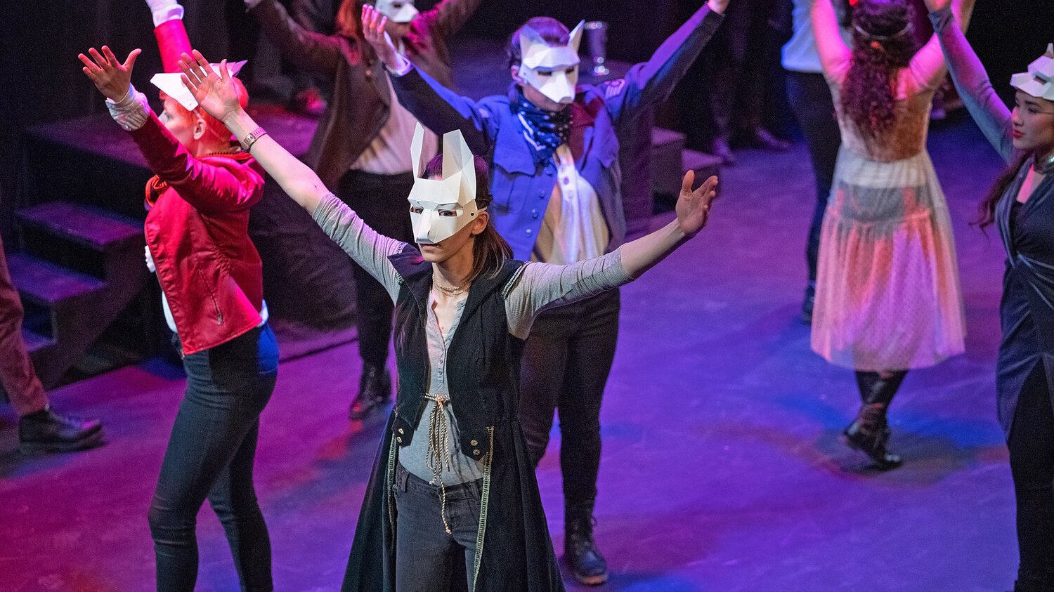Several actors performing in Romeo and Juliet are wearing white animal-like masks with ears pointing up. Their arms are in the air.