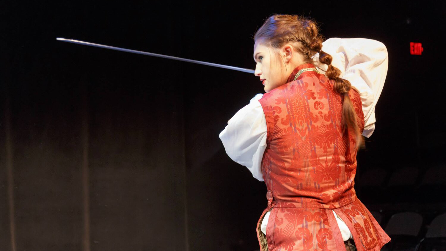 An actor performs in Richard II. The actor has their back to the camera and wields a sword.