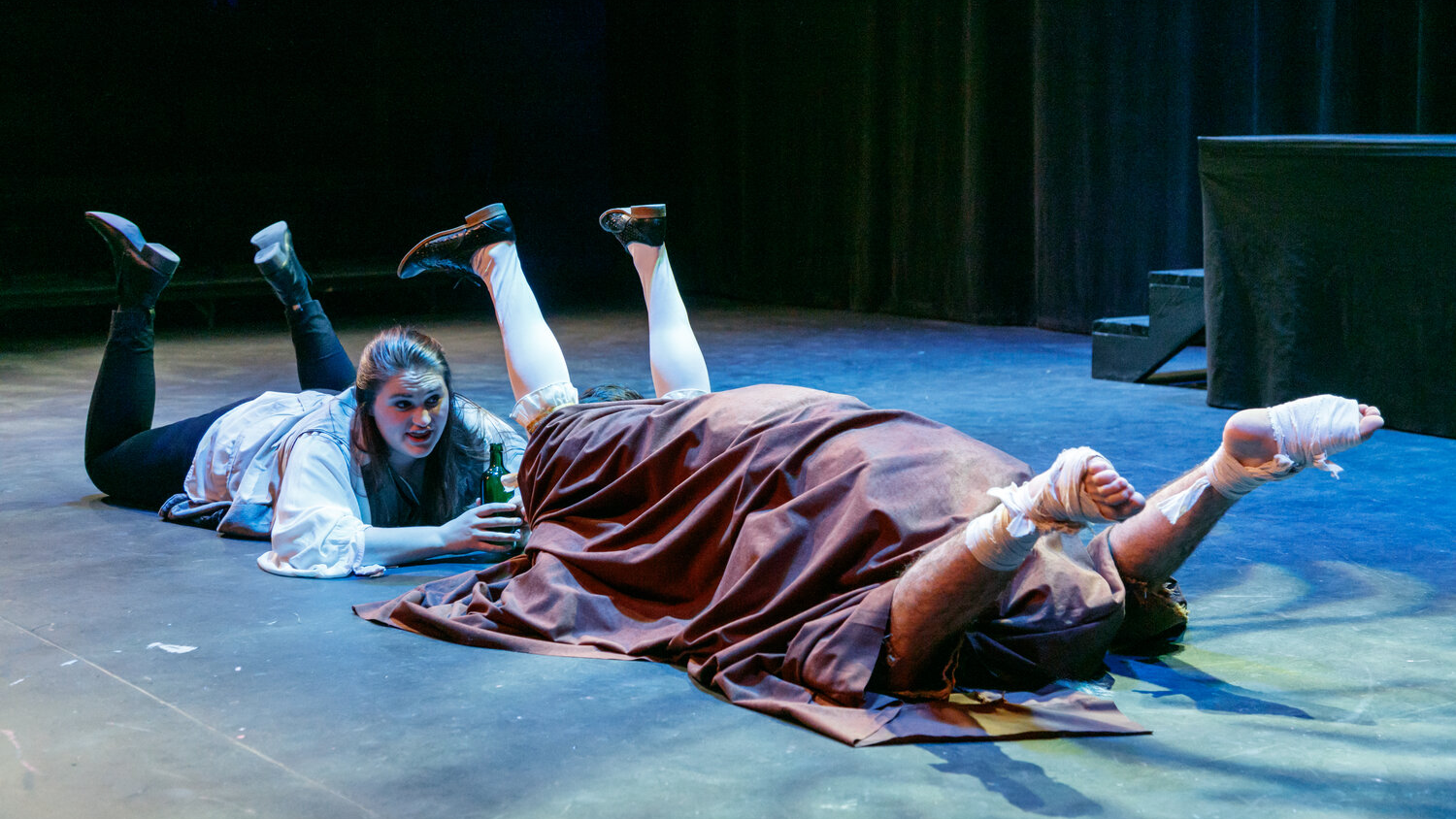 Actors perform in The Tempest. One actor lays on their stomach while two others are under a blanket with their feet in the air.