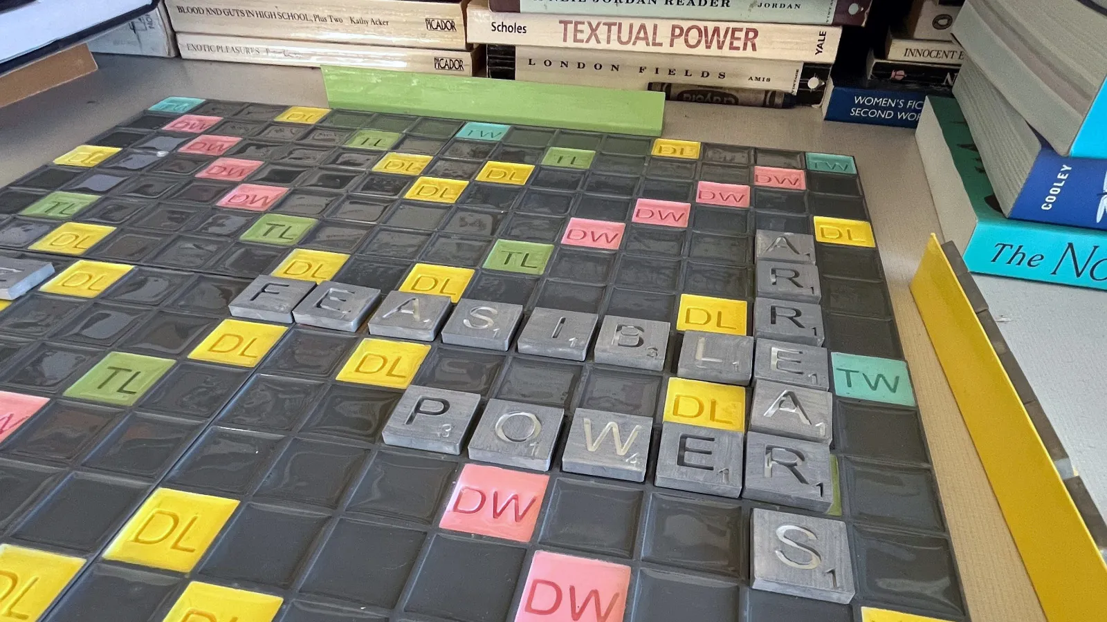 A colorful, 3D-printed Scrabble set in front of a stack of books