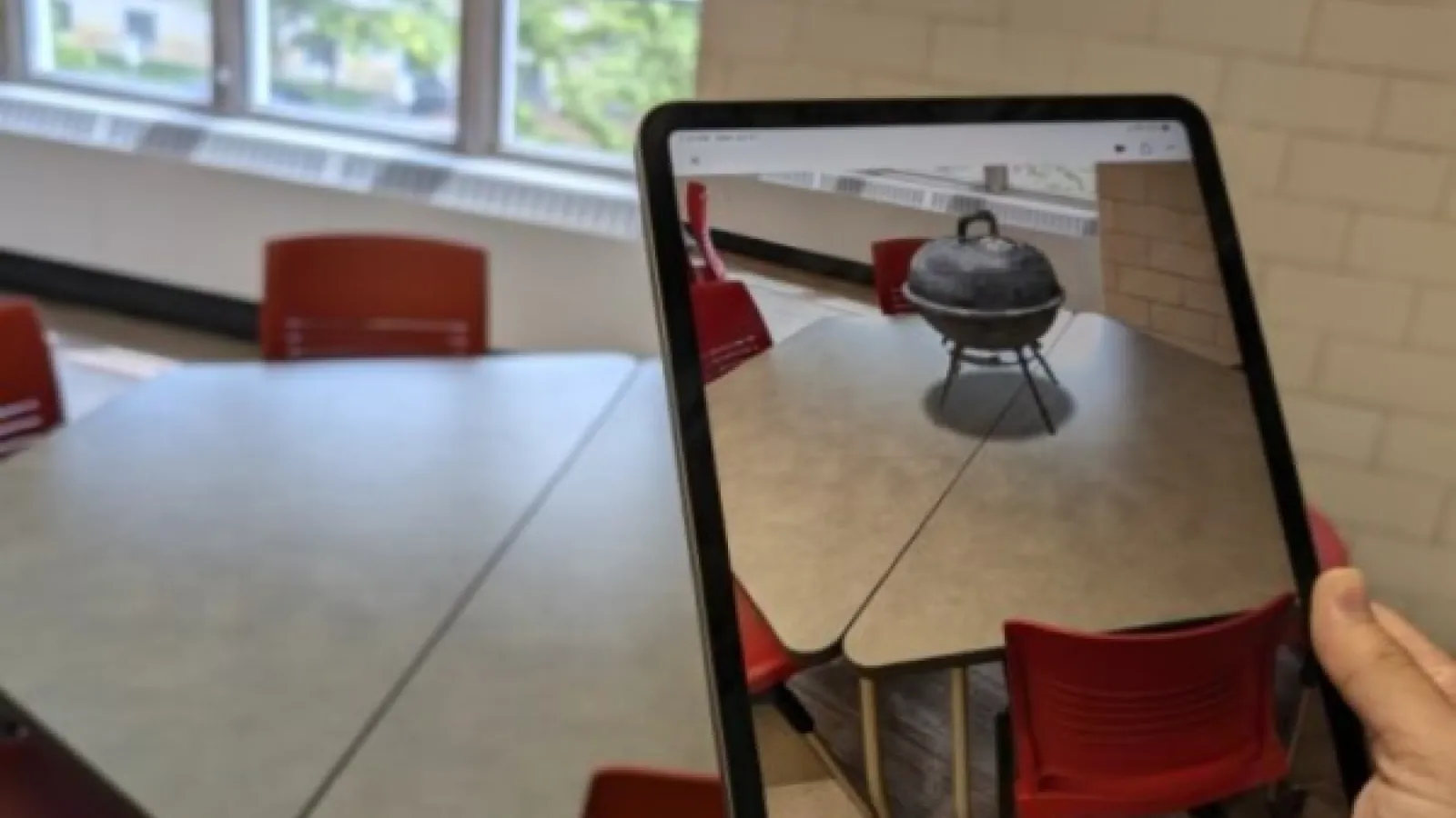 A handing holding up an iPad whose screen shows a VR grill sitting on the table behind the iPad.