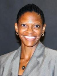 Associate Professor Andreá Williams smiles in front of a gray backdrop