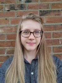 Undergraduate student Sara Bach stands, smiling, in front of a brick wall