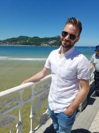 PhD candidate Joey Ferraro stands in front of a beach