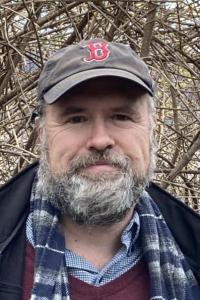 Sean O'Sullivan, wearing a Boston Red Sox baseball cap and a light scarf, looking directly at the camera with a small smile.