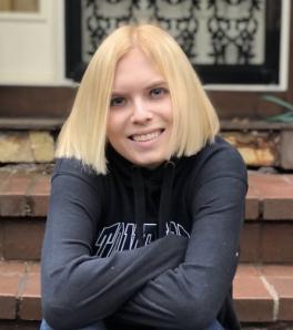 Undergraduate student Emma Deimling sits, smiling, on a brick stoop