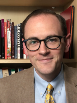 Graduate student Andrew Bashford in front of a shelf of books