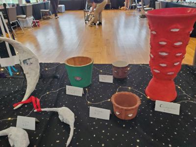 Ceramic pieces in many shapes and sizes, including a crescent moon with a face, pots with human faces and prominent nose and a large red sculpture with several white eyelets on display for sale at OUAB's Night at the Museum