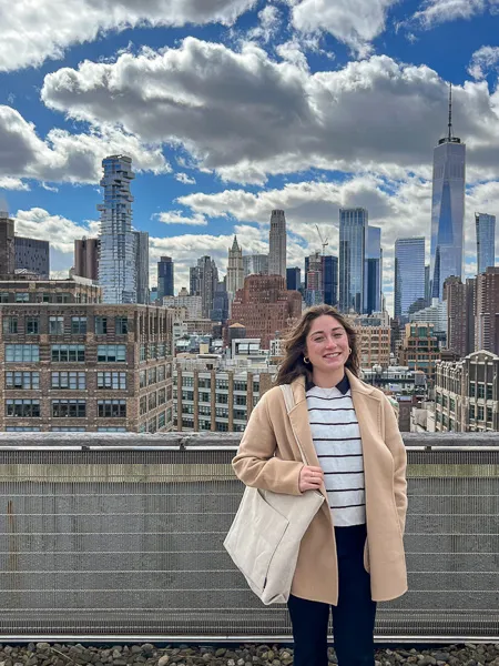 Audrey Smith stands smiling on a rooftop with the New York City skyline behind her