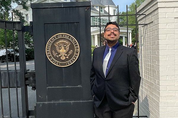 Caleb González smiles next to a pillar bearing the seal of the vice-president of the United States