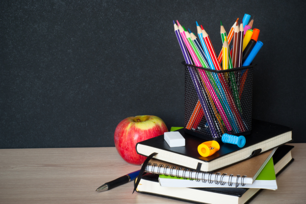 Stack of notebooks with a cup of colored pencils on top of it and an apple beside it.