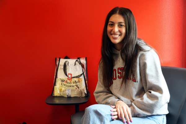 Jasmyn Maingi sits in front of a bright scarlet wall and smiles at the camera
