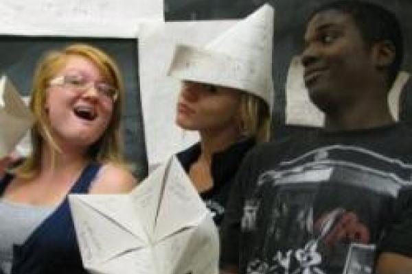 Three students goof around with folded paper hats