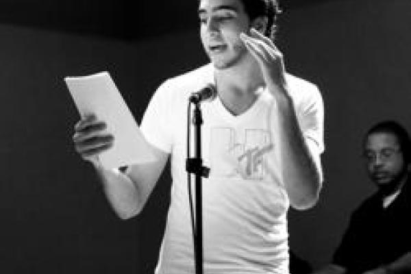 A young person at a microphone reads from a paper and gestures emphatically